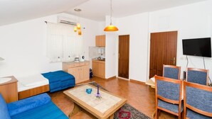En moderne stue med sofa, sofabord og lænestole. Der er et køkkenområde med skabe og et fjernsyn.