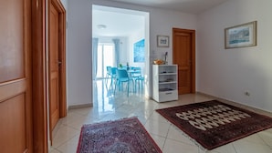 A hallway with wooden doors, a dining area with blue chairs, a white shelf unit, and two rugs. - Rooms Raic - double room - No. 1 (Dubrovnik)