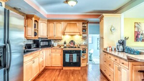Una cocina con gabinetes de madera, un refrigerador de acero inoxidable, un microondas, un horno y una cafetera.