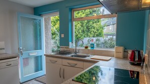A kitchen with a dishwasher, a sink, a window with a view of greenery, and a countertop with a kettle and dish soap. - Avondale Bungalow -  A cottage that sleeps 4 guests  in 2 bedrooms (Staveley)