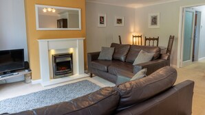 A living room with a fireplace, brown leather sofa, and a television. - Avondale Bungalow -  A cottage that sleeps 4 guests  in 2 bedrooms (Staveley)
