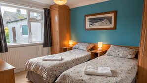 A hotel room with two beds, a window with curtains, a framed picture on the wall, and a wooden wardrobe. - Avondale Bungalow -  A cottage that sleeps 4 guests  in 2 bedrooms (Staveley)