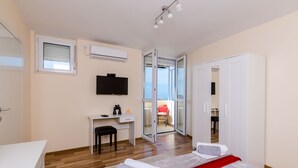 A modern bedroom with a bed, a desk, a chair, and a TV. There is a sliding glass door leading to a balcony. - Apartment Vedrana- One-Bedroom Apartment with Balcony and Sea View (Dubrovnik)