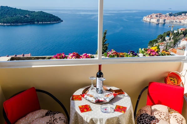 A table with a bottle of wine, glasses, and a decorative item, set against a scenic view of a coastal town and sea.