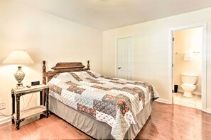 Un dormitorio con cama de madera, una mesita de noche con lámpara y una puerta que da a un baño.