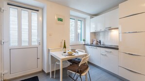 A compact kitchen with white cabinets, a dining table with chairs, and a refrigerator. - Apartments Sonja - Studio (Pucisca)