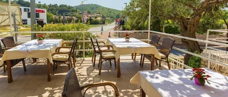An outdoor patio with tables and chairs, a pergola, and a view of a road and hills in the background.