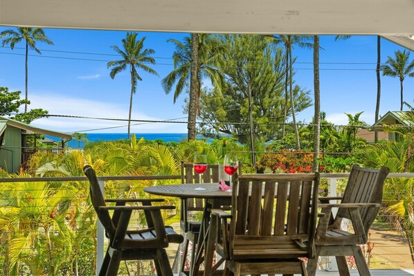 A wooden table and chairs on a balcony with a view of the ocean and palm trees. - Tropical Haena Getaway Just Steps to Beach! (Haena)