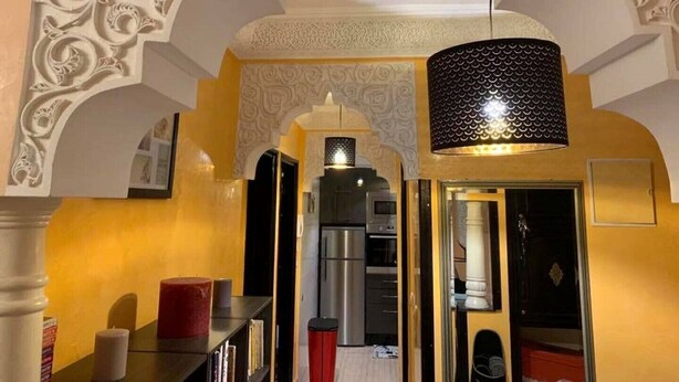 A narrow hallway with ornate wall carvings, a modern kitchen area, and a dining table with candles. - Very nice apartment F3 comfortable. (Agadir)