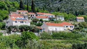 A hillside village with traditional stone houses, some with solar panels, surrounded by lush greenery and a rocky backdrop. - Guesthouse Moretic - Small Double Room with Garden View 1 (Orasac)