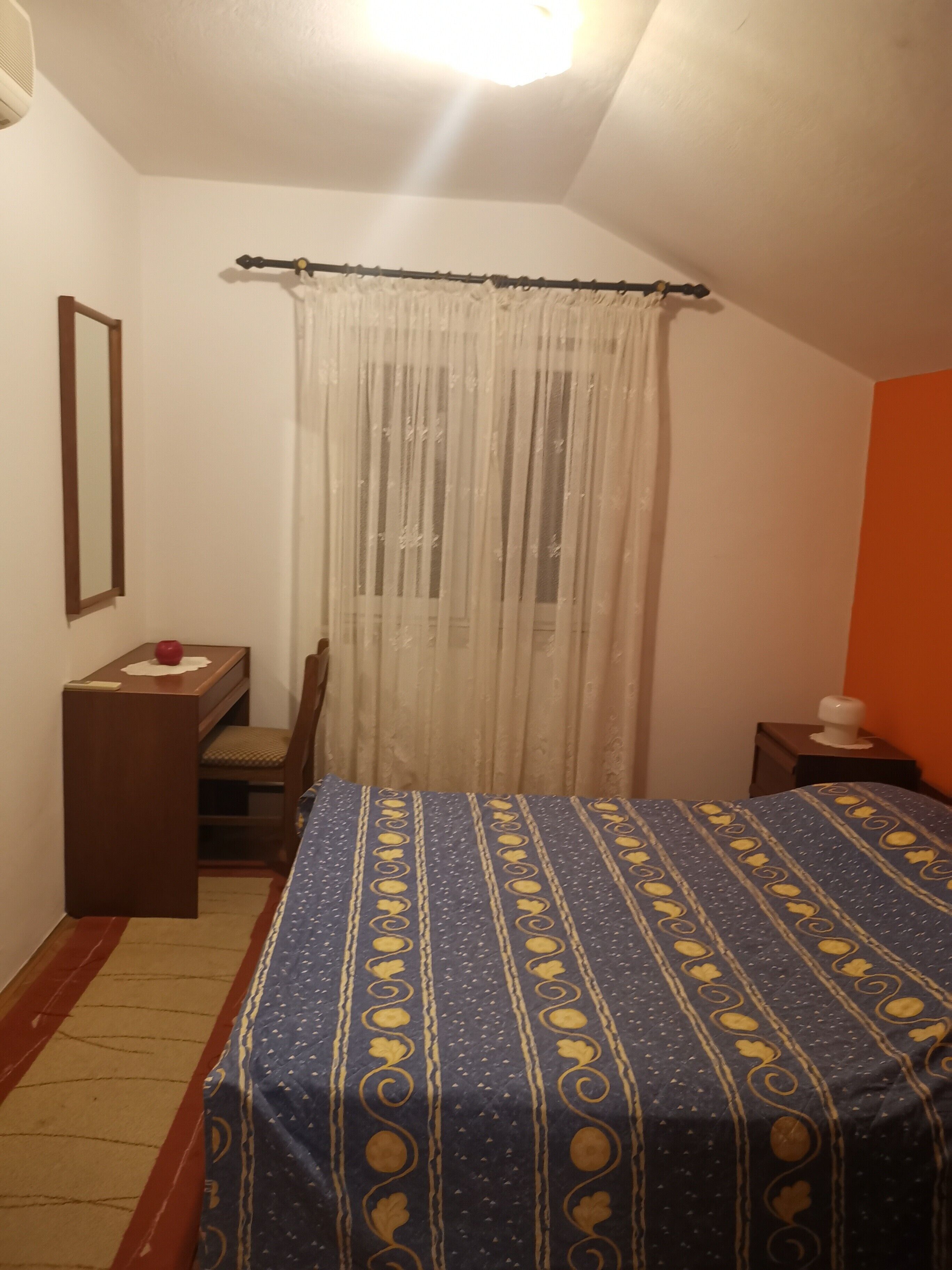 A bedroom with a bed, a chair, a small table, and a nightstand.