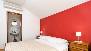 A bedroom with a bed, bedside table, lamp, and a red wall. - Guesthouse Moretic - Small Double Room with Garden View 1 (Orasac)
