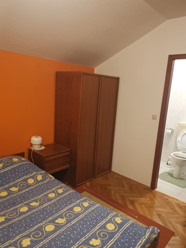 A bedroom with a bed, a wardrobe, a nightstand, and a bathroom visible through an open door.