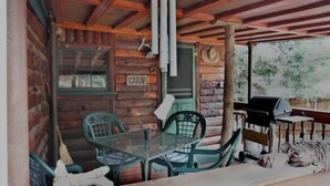 A rustic cabin with a glass table, green chairs, a wooden door labeled 'CABIN', and a barbecue grill. - Bear Creek Cabin (Ruidoso)
