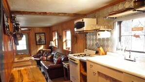 A kitchen with a stove, sink, and cabinets, a dining table with chairs, and a living area with a sofa and fireplace. - Bear Creek Cabin (Ruidoso)