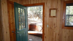 A wooden cabin with a green door, a bed, and a hot tub visible through the door. - Bear Creek Cabin (Ruidoso)