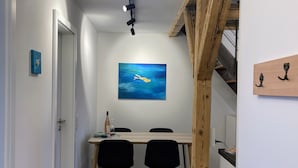 A modern dining area with a wooden table and chairs, a painting on the wall, and a staircase with exposed beams.