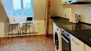 A compact kitchen with wooden beams, a washing machine, and a window with a view.