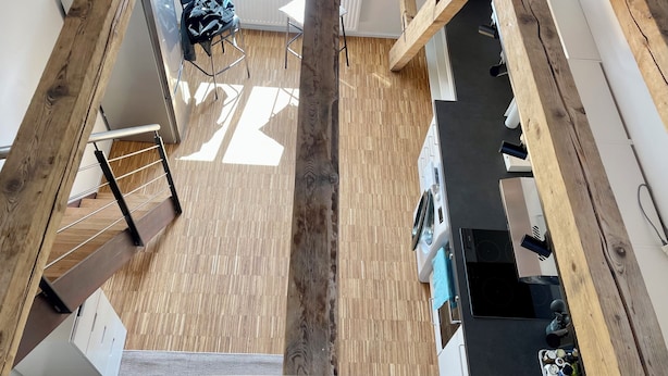 A modern kitchen with wooden beams, a dining area with a table and chairs, and a staircase with a metal railing.