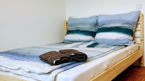 A single bed with a wooden frame, a blue and white bedding set, two pillows, and a pair of folded towels on the bed.