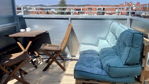 A balcony with a wooden table, a folding chair, and a blue cushioned sofa.