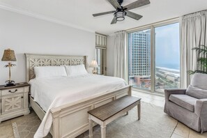 Une chambre avec un grand lit, une table de chevet, un banc, une chaise et une vue sur le paysage urbain, visible à travers de grandes fenêtres.