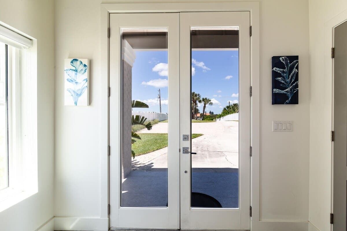 Una puerta blanca con paneles de vidrio, una pequeña ventana a la izquierda y dos cuadros en la pared.