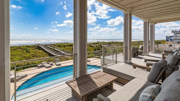 A covered outdoor area with a pool, lounge chairs, and a view of the ocean.