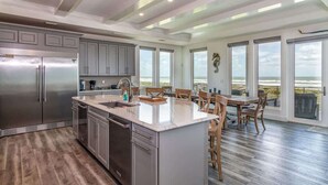 A modern kitchen with a large island, stainless steel appliances, and a view of the ocean through large windows.