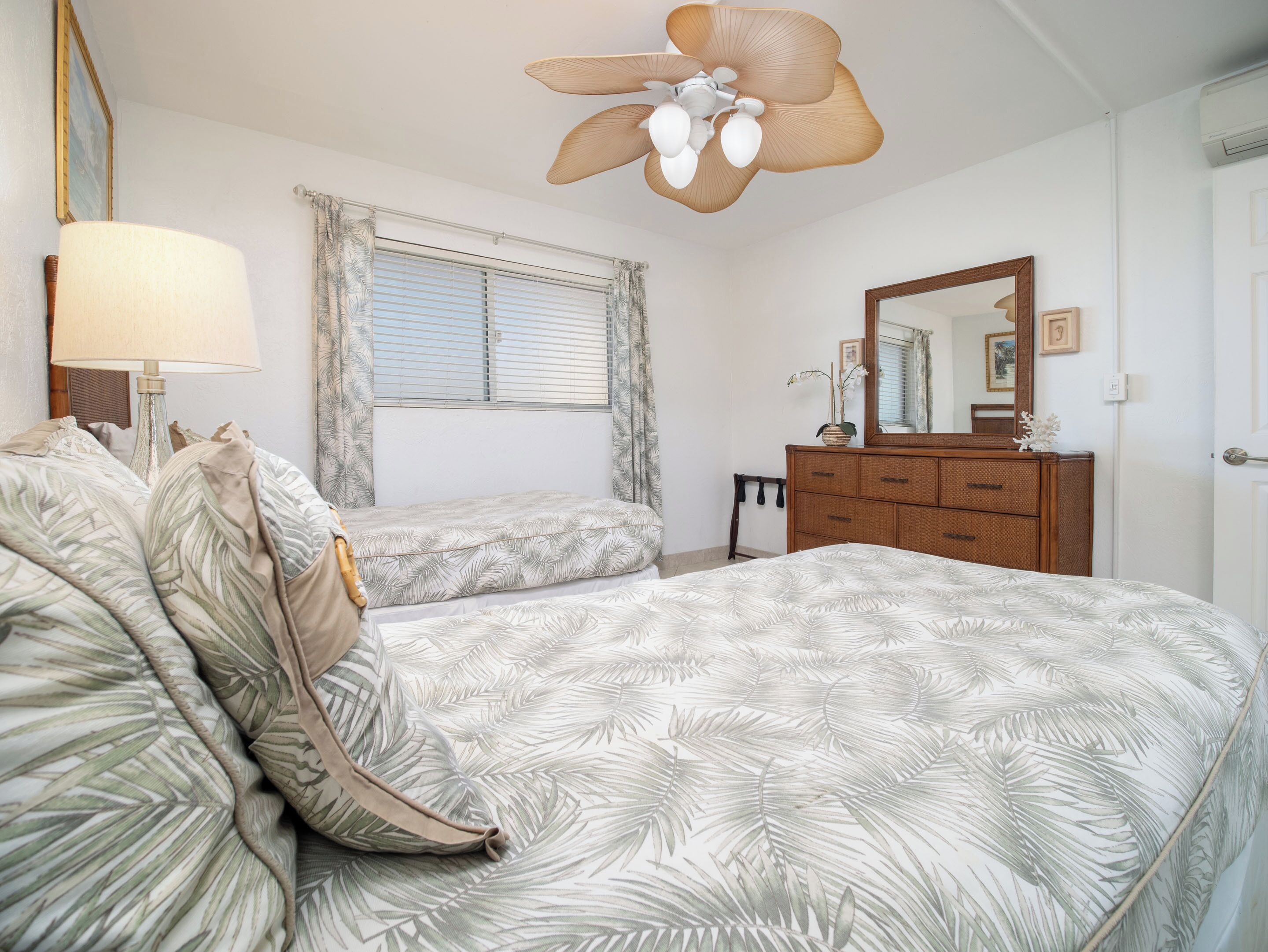 Ein Schlafzimmer mit Bett, Schminktisch, Spiegel, Deckenventilator und Fenster mit Vorhängen.