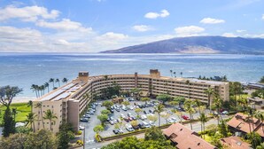 Un hotel con un edificio curvo, aparcamiento y vistas al océano y a las montañas.