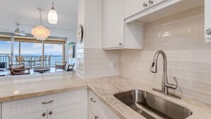 Una cocina moderna con un amplio ventanal, armarios blancos y un lavamanos de acero inoxidable.