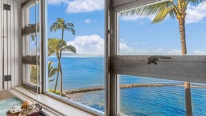 Una habitación con un ventanal grande que da a una playa con palmeras y agua azul cristalina.