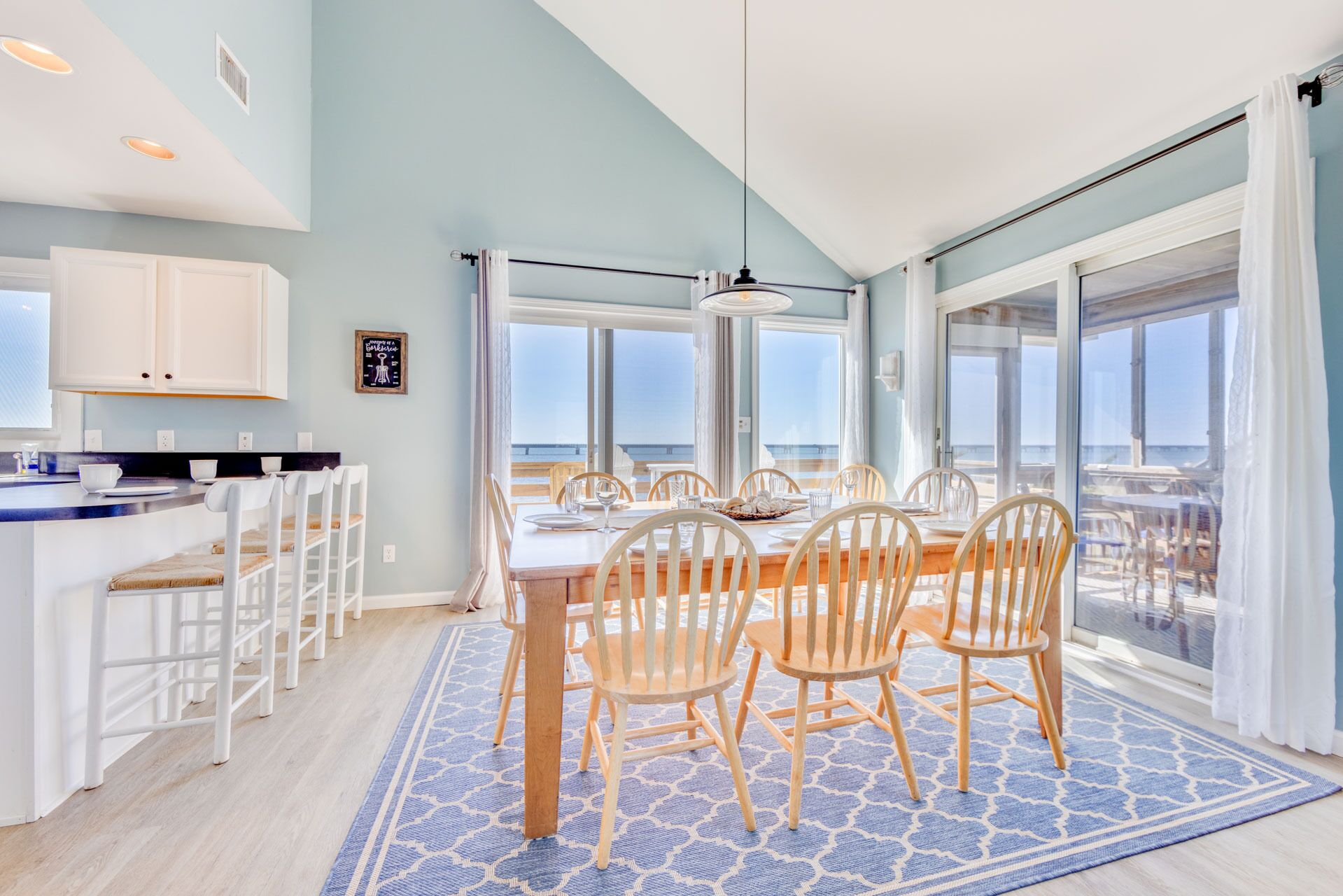 A dining area with a view of the beach, a kitchen with white cabinets, and a large window.