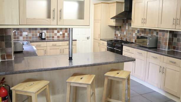 A kitchen with wooden cabinets, a tiled backsplash, a gas stove, a toaster, and two wooden stools. - Right Stays (Guildford)