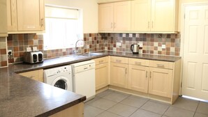 A kitchen with wooden cabinets, a washing machine, a toaster, and a tiled backsplash. - Right Stays (Guildford)
