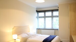 A bedroom with a bed, bedside lamp, window with blinds, and a radiator. - Right Stays (Guildford)