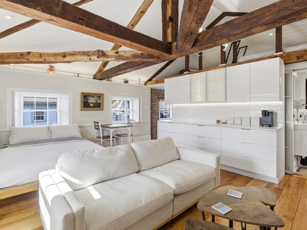 Ein modernes Zimmer mit Bett, Sofa, Esstisch und Küchenzeile.