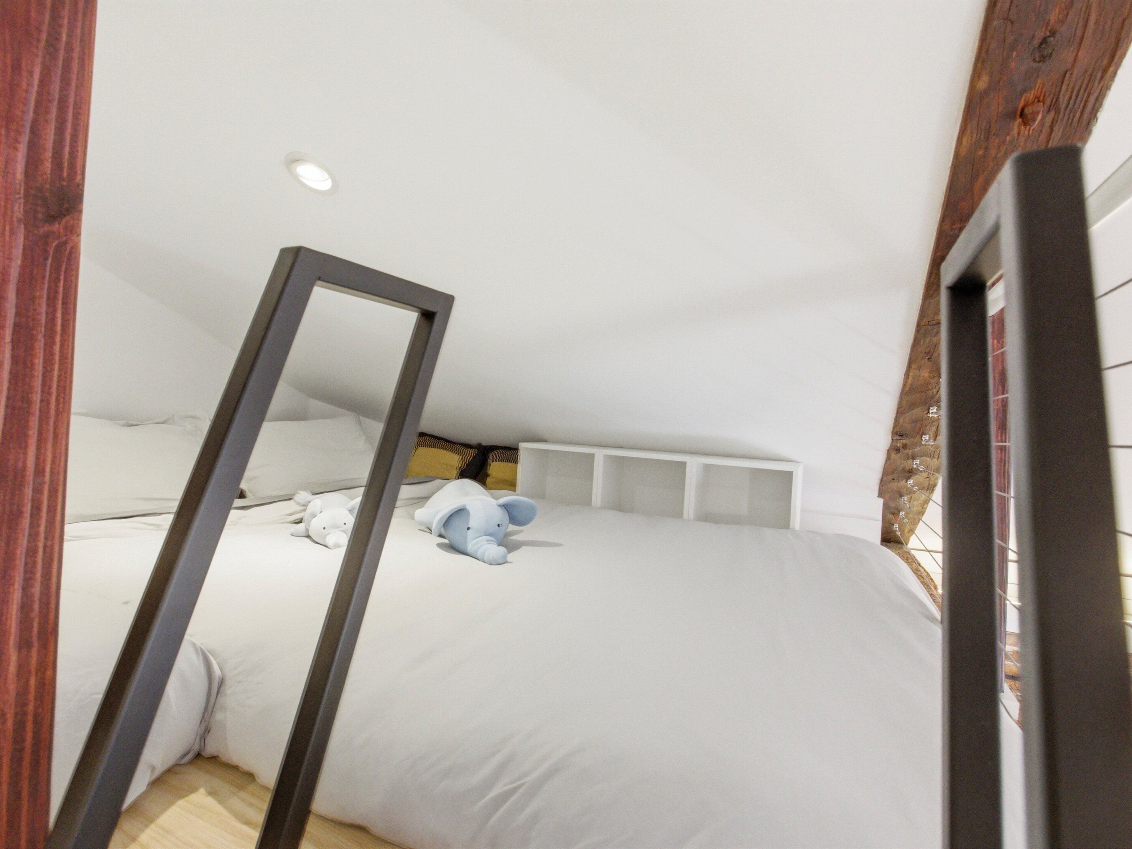 A bedroom with a sloped ceiling, a bed with white bedding, a bedside table, and a mirror.