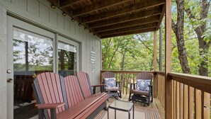 A covered porch with a wooden bench and two Adirondack chairs, a small table, and a rug.