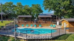 A pool area with a fenced deck, lounge chairs, and a small building with a roof.