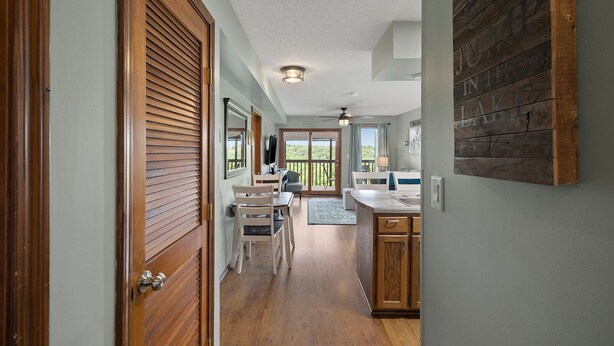 A hallway leading to a dining area with a view of the outdoors, wooden doors, and a kitchen area with a wooden accent wall.