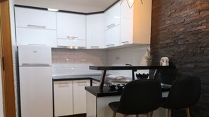 Una cocina compacta con armarios blancos, encimera negra y pared de ladrillo decorativa. Hay dos taburetes negros y una pequeña isla con estufa.