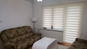 Una sala de estar con un sofá estampado con motivos florales, un reposapiés blanco y un radiador.