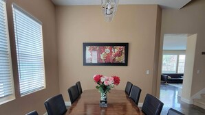Uma sala de conferências com uma longa mesa de madeira, cadeiras de couro preto, um candelabro e uma obra de arte floral emoldurada na parede.