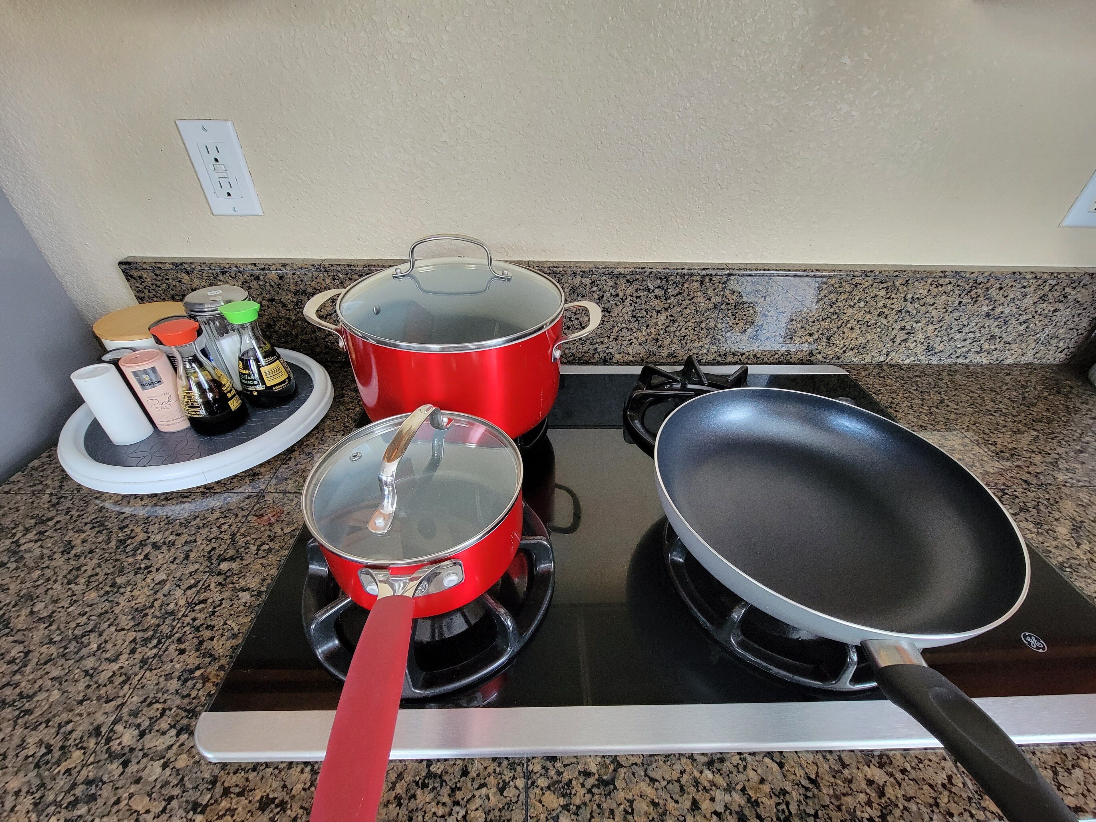 A kitchen with a gas stove, two red pots, a frying pan, and a tray with condiments.