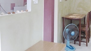 A room with a wooden table and chairs, a standing fan, and a door leading to another room.