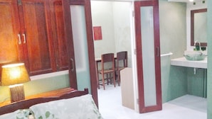A bedroom with a bed, a nightstand, a lamp, a wardrobe, and a bathroom with a sink and mirror.