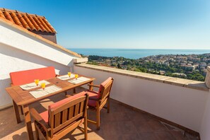 Une terrasse avec une table et des chaises en bois, donnant sur une ville côtière.