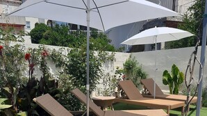 A rooftop garden with artificial grass, lounge chairs, and umbrellas.
